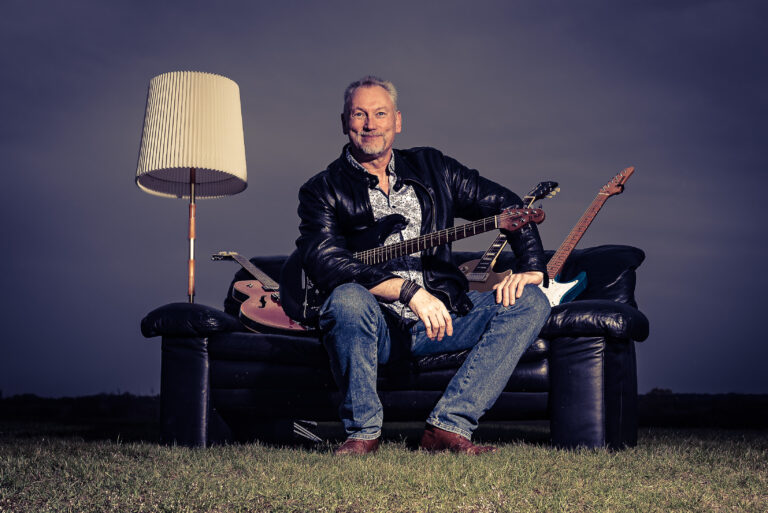 Typ mit mehreren Gitarren auf einem Sofa